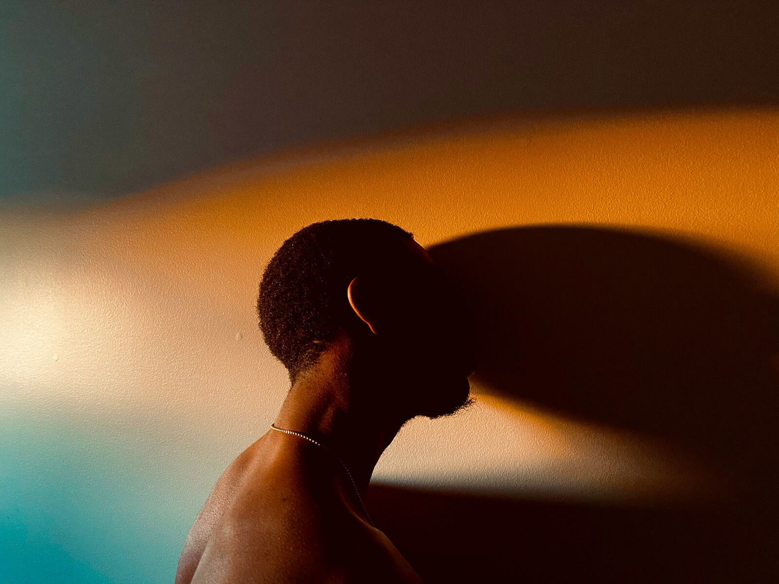 Man standing in dark room, with head resting against wall.